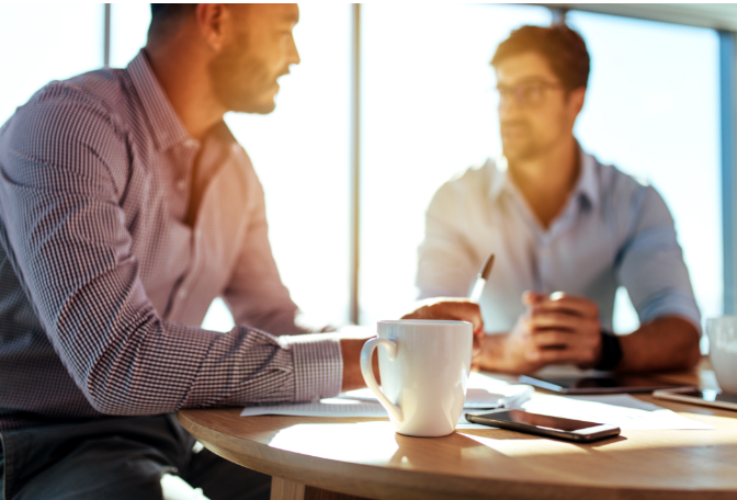 Two men sat at a table talking to eachother